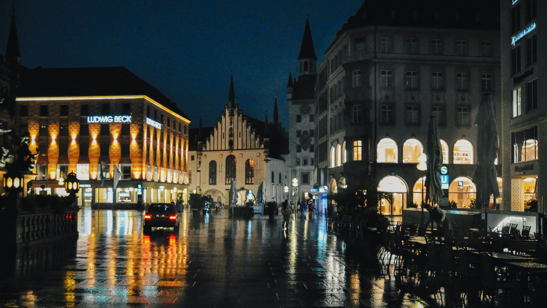 Regnerische Stadtstraße bei Nacht mit beleuchteten Gebäuden und Spiegelungen